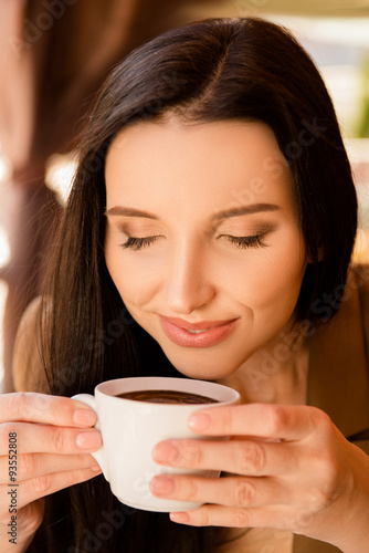 Charming young woman enjoying aroma coffee in cafe