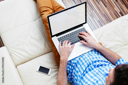 Slika na platnu Man sitting on a sofa and browsing the web