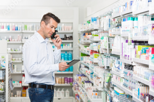 Customer Using Mobile Phone And Digital Tablet In Pharmacy