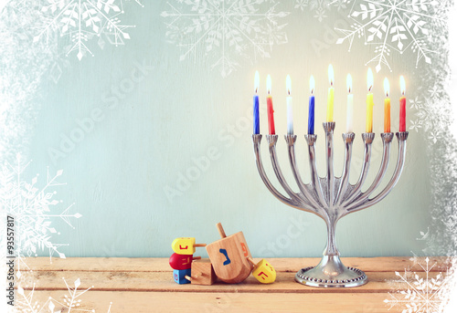 image of jewish holiday Hanukkah with menorah (traditional Candelabra) and wooden dreidels (spinning top). glitter and snowflakes overlay
