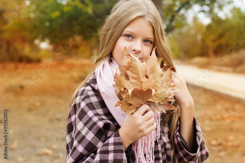 Cute girl is holding maple leaves near face