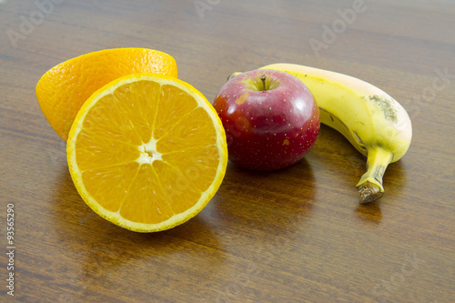 Combination of fruit over a wooden table: sliced orange, apple and banana