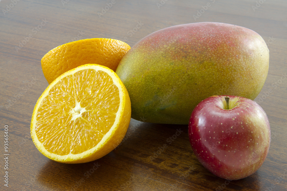 Combination of fruit over a wooden table: sliced orange, mango and apple Combination of fruit over a wooden table: sliced orange, mango and apple