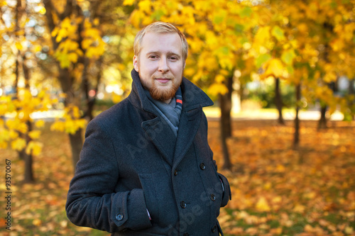 a man dressed in a dark coat and scarf in autumn park
