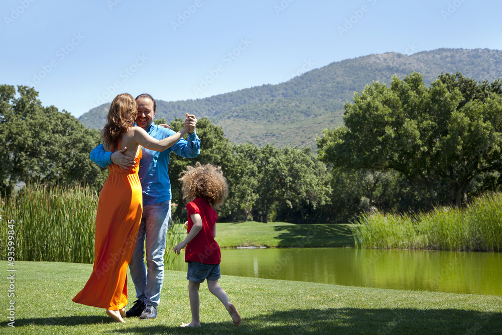 Obraz premium Happy parents are dancing on grass at park on a weekend day all together