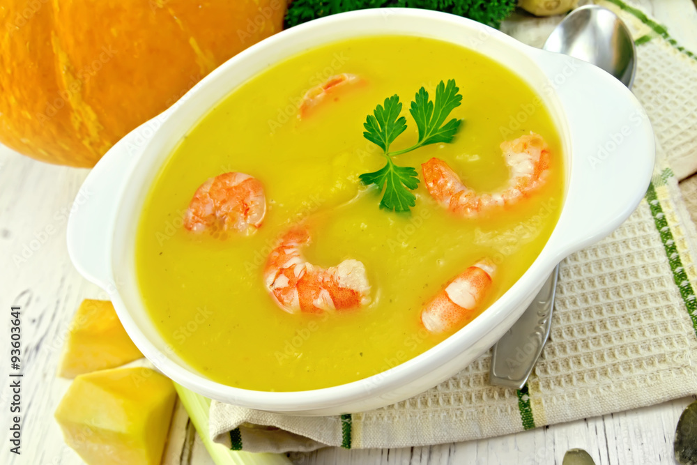 Soup-puree pumpkin with shrimp in white bowl on board
