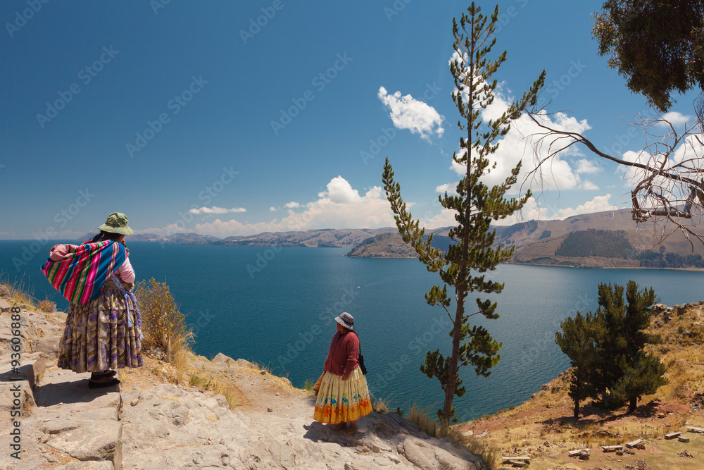 Obraz premium Two Women In Traditional Bolivian Clothes Standing On The Rock Close To The Titicaca Lake.
