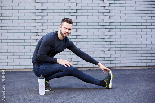 Sport man with beard stretching against concrete wall