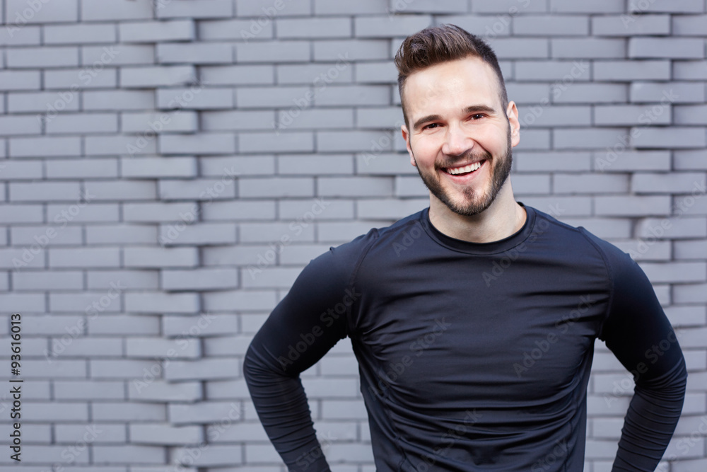 Smiling male runner in t-shirt standing against cement wall background Smiling male runner in t-shirt standing against cement wall background