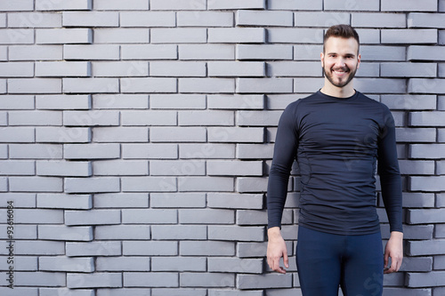 Smiling male runner in t-shirt standing against cement wall background