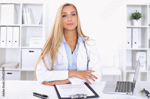 Blonde female doctor sitting at the table in hospital