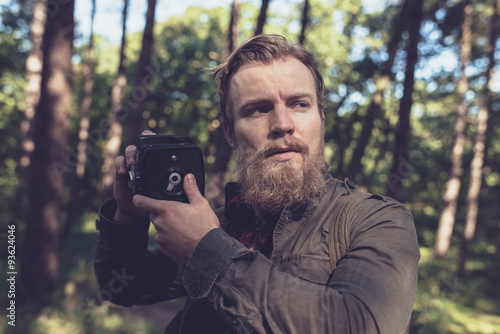 Alert beard man holding vintage camera in forest.
