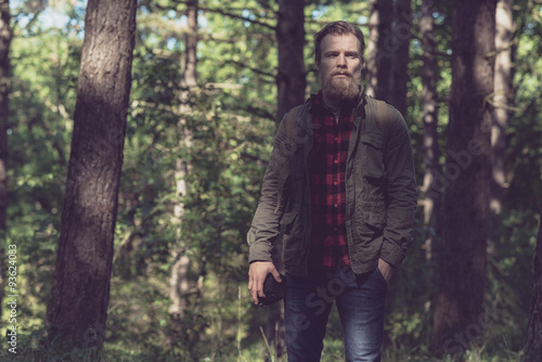 Observing beard man holding vintage camera in forest.