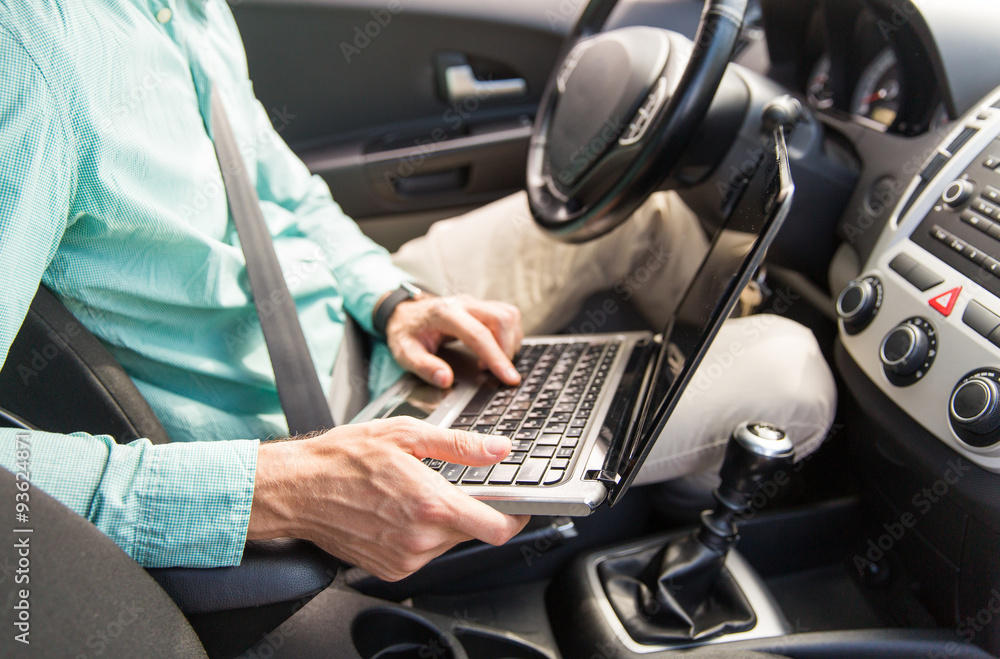 close up of young man with laptop driving car close up of young man with laptop driving car