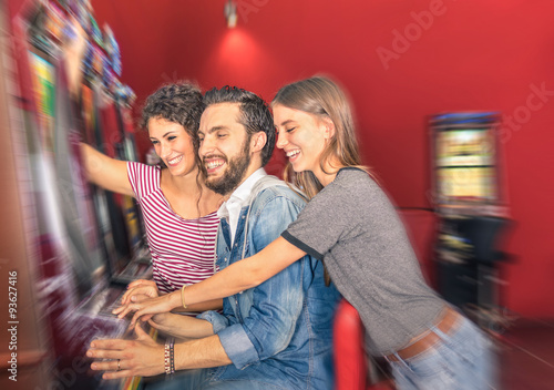 Happy young friends having fun together with slot machine - Gambling concept with people playing at cash automatic devices in modern casino and resort - Blurred edges with soft radial zoom defocusing