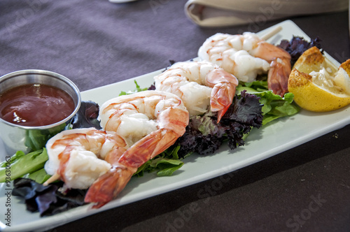 shrimp appetizer at a gourmet restaurant with sauce on a bed of lettuce and lemon slice