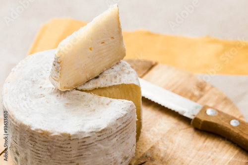 whole caciotta cheese with slice over chopping board and knife