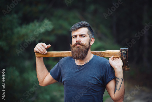 brutal brunette bearded man with a hatchet in the woods on a background of trees