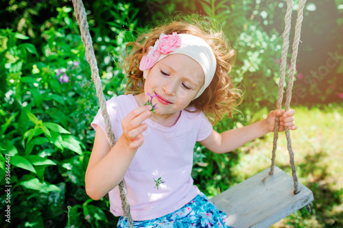 child girl on swing on summer vacation in the garden