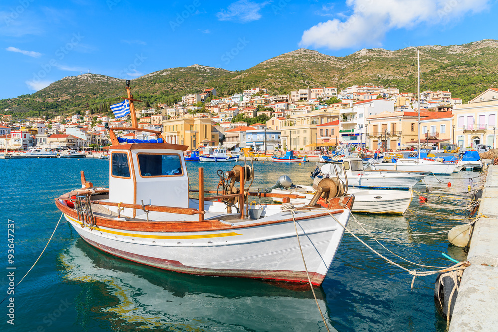Traditional Greek boat in port of Samos with colourful houses in background, Greece