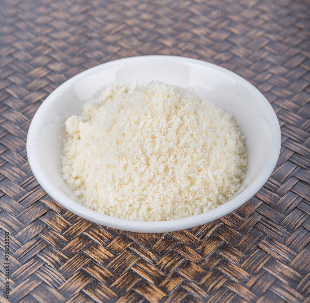 Grated cheese in white bowl over wicker background
