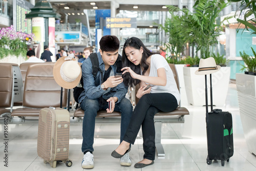 Young Asian couple using smart phone while sitting in the airpor photo