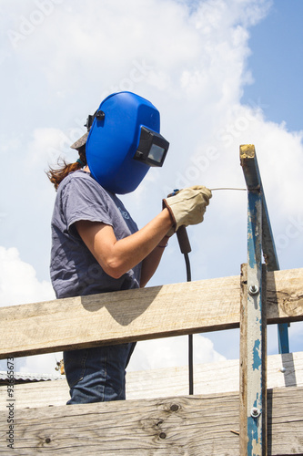 Female welder mending fence on farm wearing welding helmet