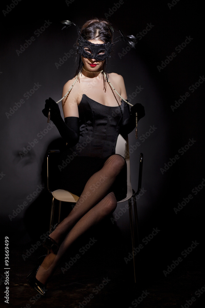 Beautiful and mysterious masked young woman on black background