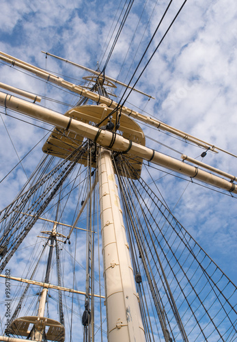 Wooden sailship rigging against blue sky with clouds
