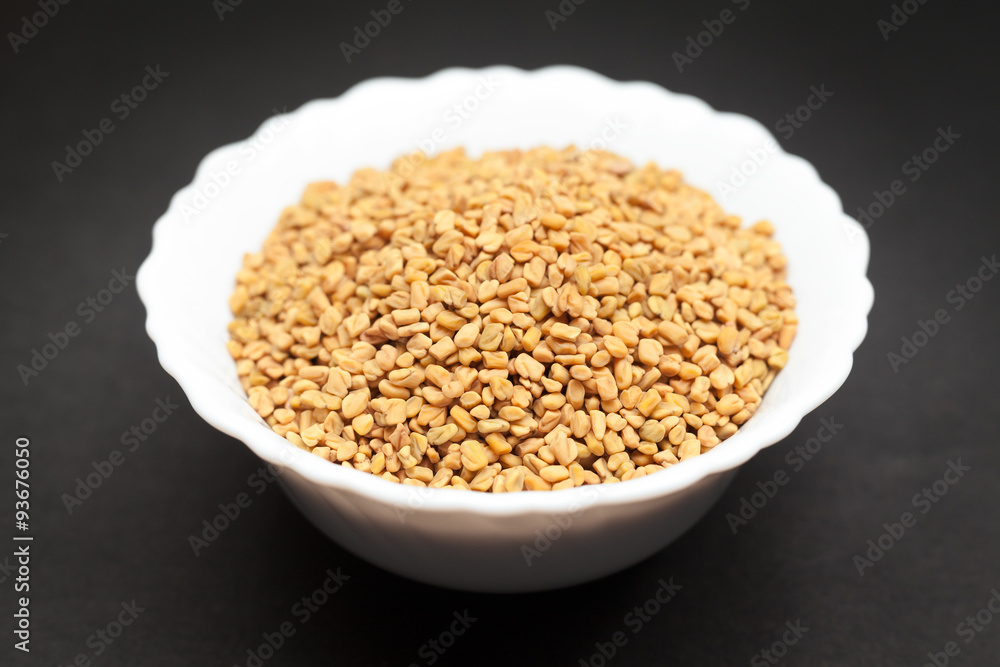 Organic Fenugreek (Trigonella foenum-graecum) in white ceramic bowl on dark background. Organic Fenugreek (Trigonella foenum-graecum) in white ceramic bowl on dark background.