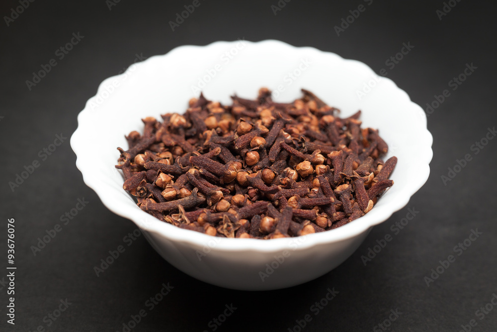 Organic black clove (Syzygium aromaticum) in white ceramic bowl on dark background. Organic black clove (Syzygium aromaticum) in white ceramic bowl on dark background.