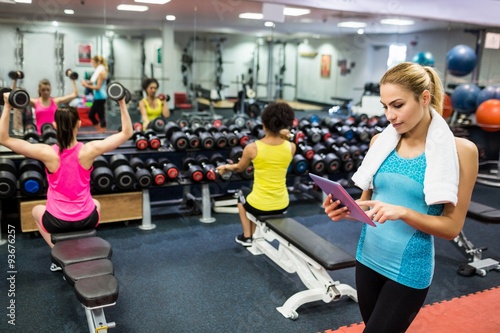 Fit woman using tablet in weights room