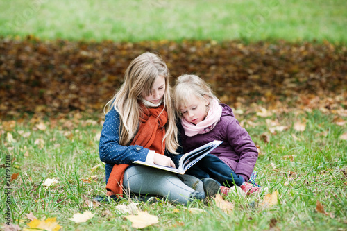 Two girls reading a book in the autumn park
