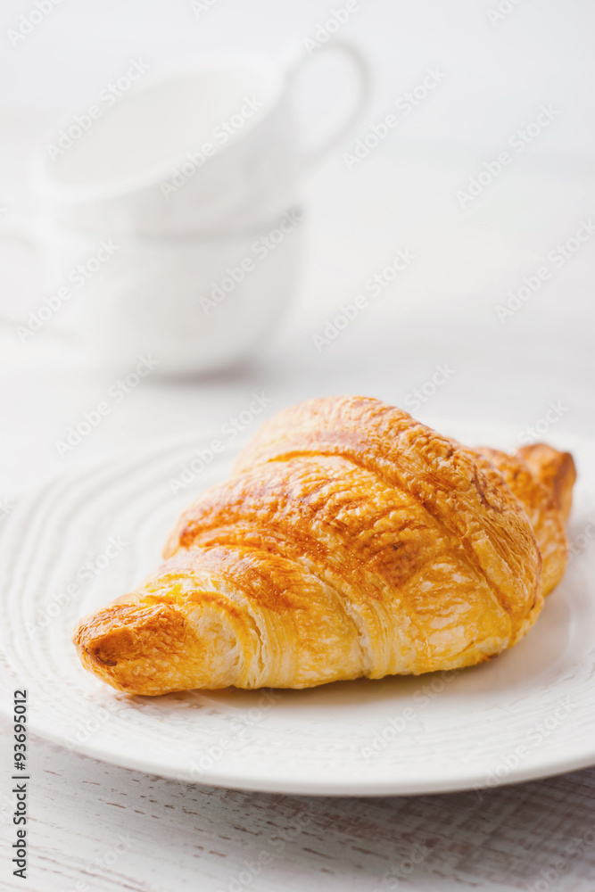 Croissant on the white plate with two blurred cups Croissant on the white plate with two blurred cups