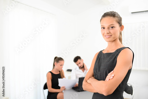 portrait of an attractive young business woman standing in office with working partner in background