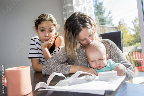 Mother holding baby  and typing on laptop computer in kitchen. photo