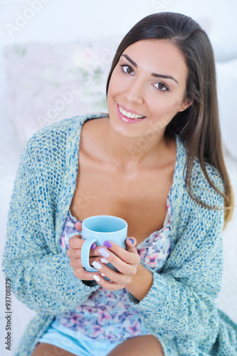 Portrait of a smiling beautiful woman sitting in bed with a cup of morning coffee