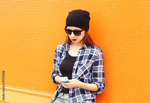 Fashion pretty cool girl using smartphone in city over orange ba