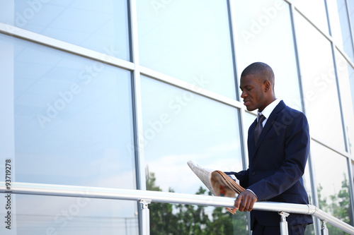 Handsome African American businessman with newspaper near business centre