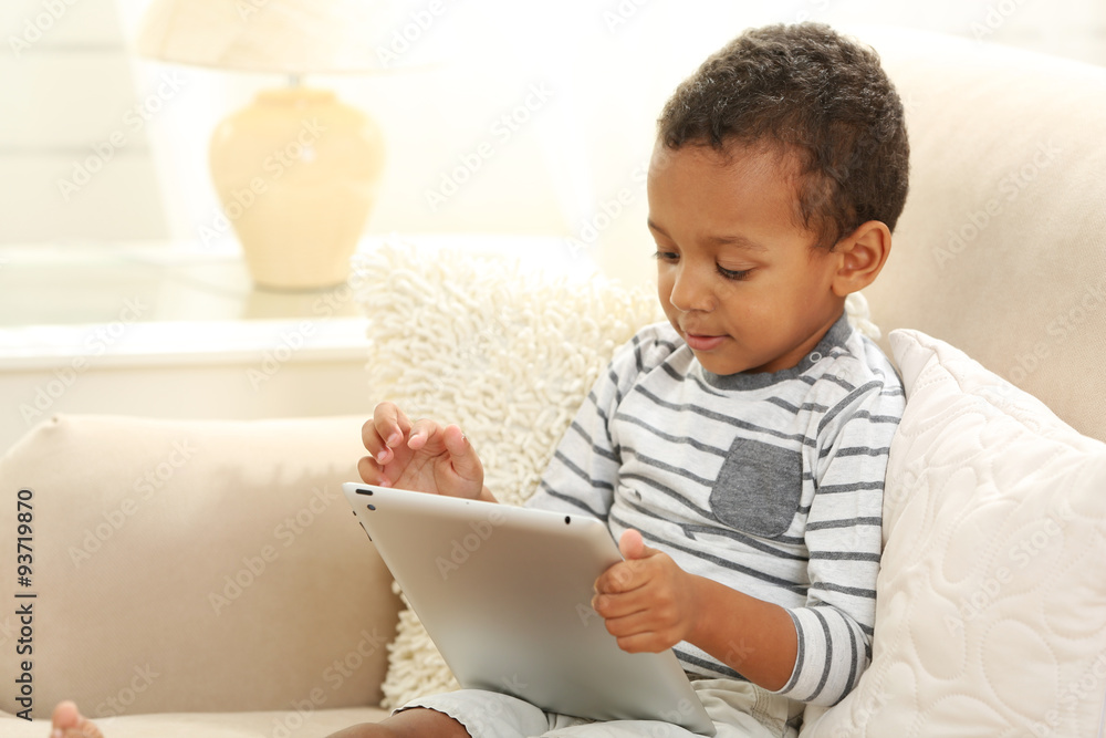 Little boy sitting on sofa with tablet in the room