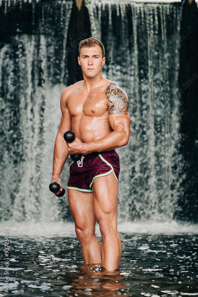 Muscular man lifting dumbbell on waterfall Muscular man lifting dumbbell on waterfall