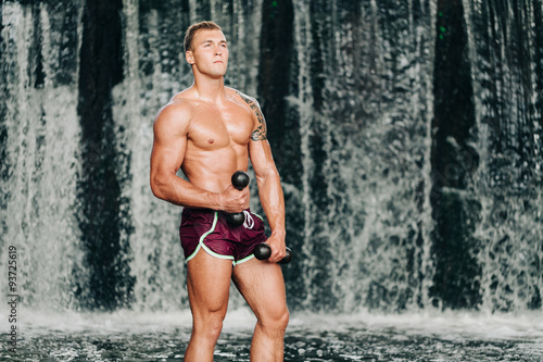 Muscular man lifting dumbbell on waterfall