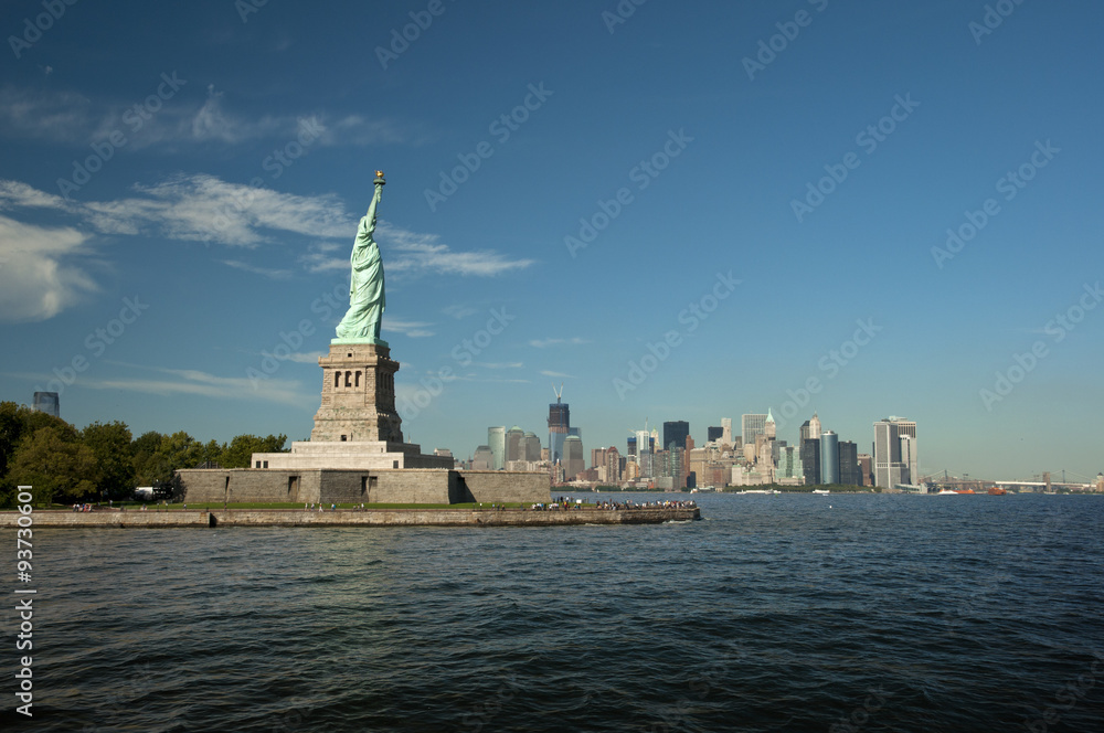Statue of Liberty on Liberty Island in front of the Manhattan Skyline on a summer day with blue sky, New York City, USA