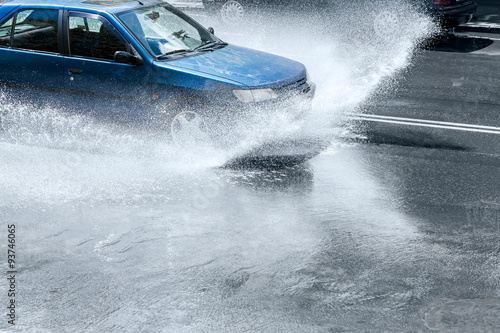 car splashes through large puddle on wet road