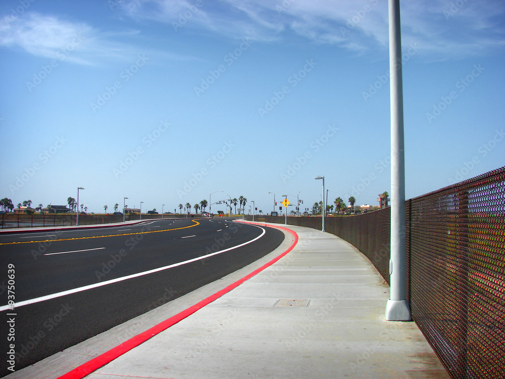 road and red curb on sidewalk leading to beach with blue sky