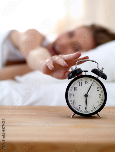 Young sleeping woman and alarm clock in bedroom at home