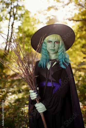 Young girl with green hair and broom in suit of witch in forest. Halloween time