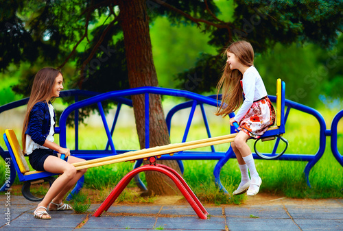 cute girls having fun on seesaw at playground photo