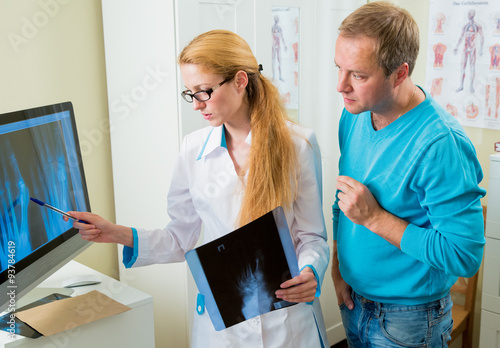 Worried female doctor with handsome male patient looking at x-ray at office. Doctor talking to her patient and showing radiograph.