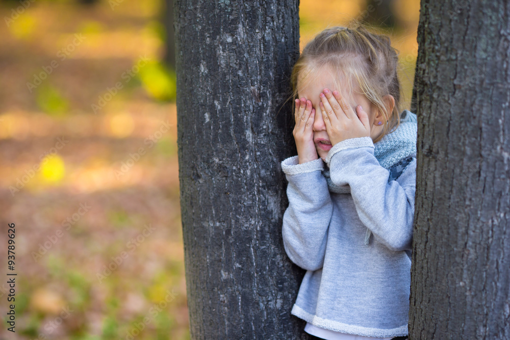 Little girl playing hide and seek near the tree in autumn park Little girl playing hide and seek near the tree in autumn park